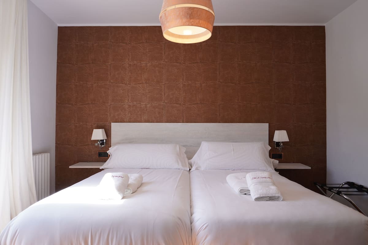 Et hotelværelse med to senge, hvide sengetæpper, en væg med brun struktur og en hængende lampe.