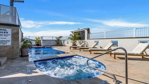 Una piscina en la azotea con sillas de descanso, un jacuzzi y un letrero con las normas de la piscina.