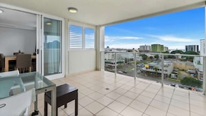 A balcony with a city view, a dining area with a glass table, and a sliding glass door. - McLeod Rise—Cairn Base with Rooftop Pool & Spa (Cairns)