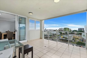 A balcony with a city view, a dining area with a glass table, and a sliding glass door.