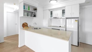 A modern kitchen with white cabinetry, a central island with a sink, and a built-in oven. - McLeod Rise—Cairn Base with Rooftop Pool & Spa (Cairns)