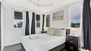 A hotel room with a bed, a nightstand, a ceiling fan, and a window with curtains. - McLeod Rise—Cairn Base with Rooftop Pool & Spa (Cairns)