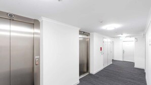 A hallway with two elevators, white walls, and a grey carpet. - McLeod Nook—Poolside Studio by Waterfront & Market (Cairns)