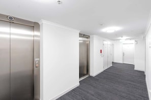 A hallway with two elevators, white walls, and a grey carpet.