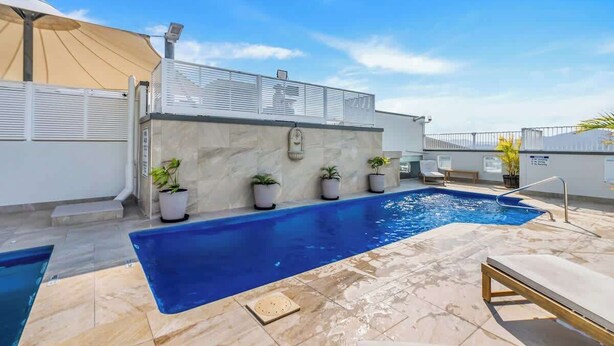 A swimming pool with a sunshade, potted plants, and a lounge chair. - McLeod Nook—Poolside Studio by Waterfront & Market (Cairns)