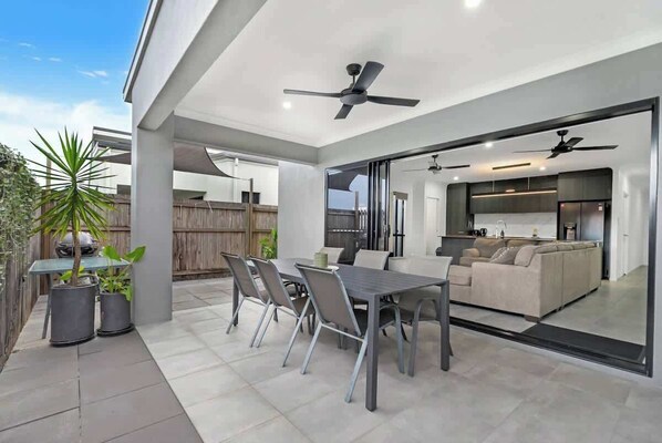 An outdoor patio with a dining table and chairs, a sofa, and ceiling fans.