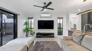 Un salon moderne doté d’un téléviseur à écran plat, d’un ventilateur de plafond et d’une grande fenêtre.