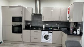 Une cuisine compacte dotée d’appareils électroménagers intégrés, d’un lave-linge et d’un banc gris.