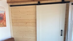 Ein Zimmer mit braun-ledrigem Sofa, einer Holzwand, einer weißen Tür und einem Vorhang.