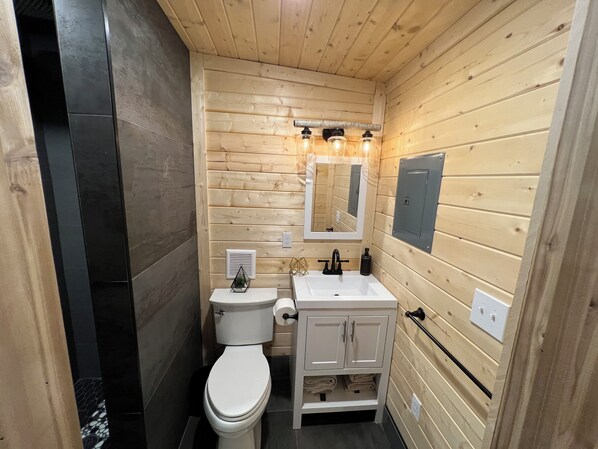 A compact wooden bathroom with a toilet, sink, and mirror.
