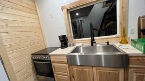 Eine Küche mit Holzausstattung, einem Edelstahlspülbecken, einer Kaffeemaschine und einem Fenster über dem Spülbecken.