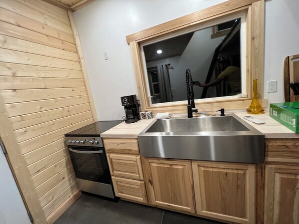 Une cuisine avec des meubles de rangement en bois, un évier en acier inoxydable, une machine à café et une fenêtre au-dessus de l’évier.