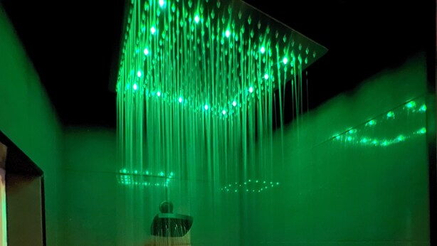 Ein Zimmer mit beleuchtetem Wasserspiel, einem Waschbecken und einem gerahmten Bild an der Wand.