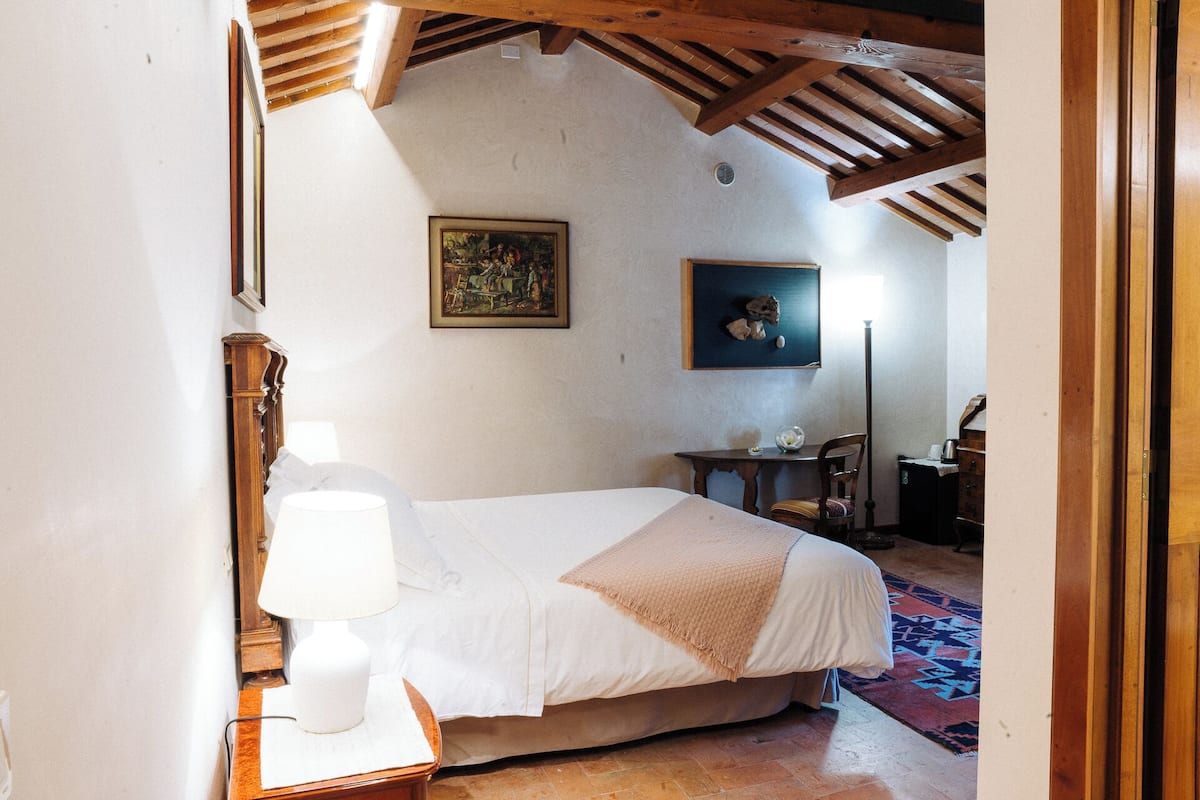 Une chambre à coucher avec un lit, une table de chevet, une lampe, un tableau et une petite table avec une chaise.