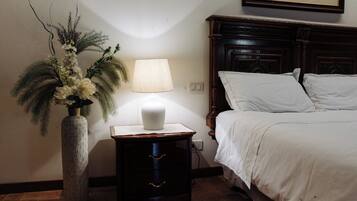 A bedroom with a bed, a nightstand with a lamp, and a decorative vase with flowers.