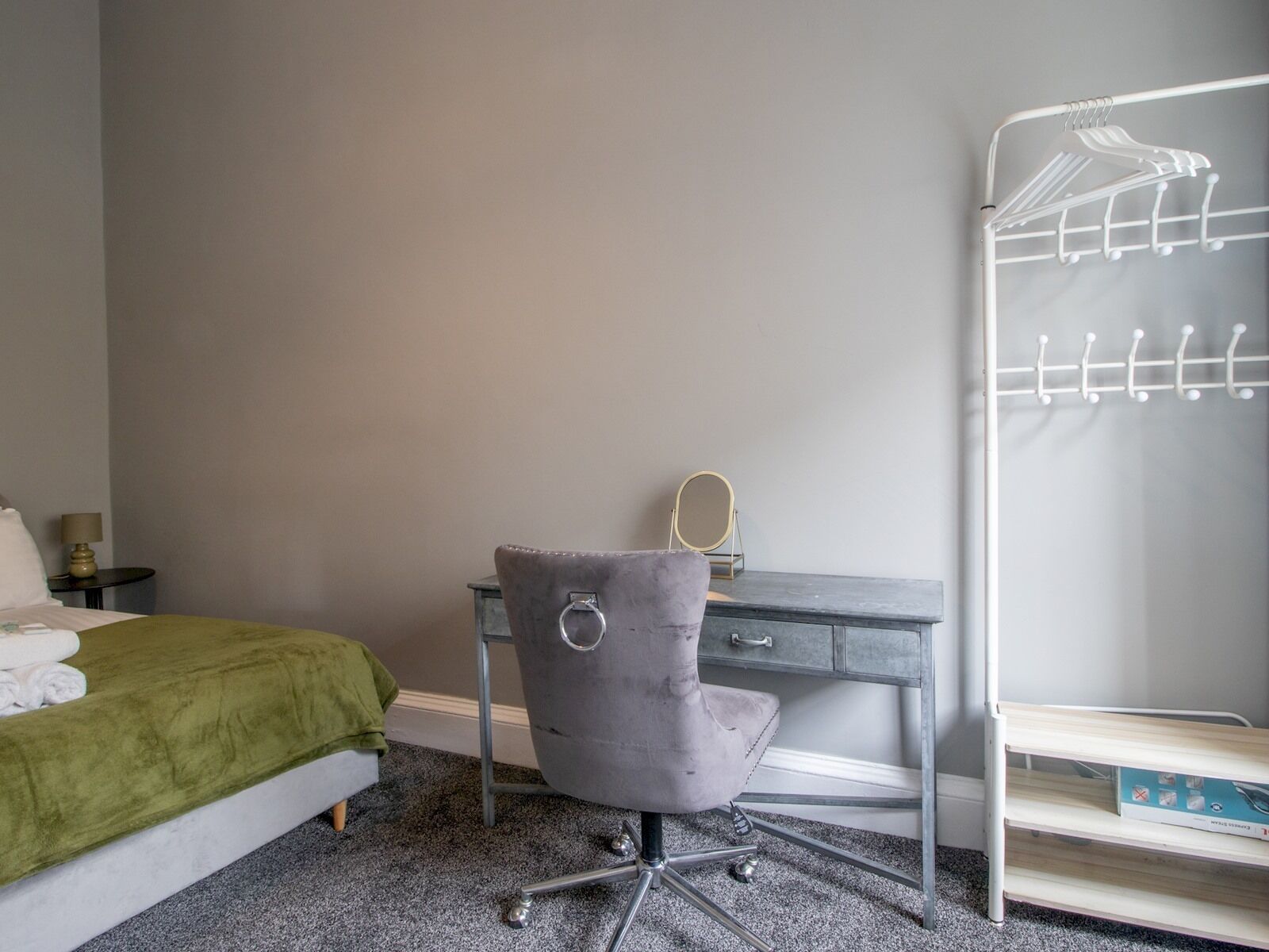 A bedroom with a bed, a desk, a chair, a vanity, and a wardrobe.