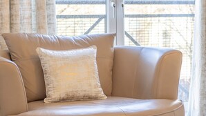 A tan leather sofa with a textured pillow in a room with a large window and curtains. - Pass the Keys | Next to Braehead - Free Parking (Renfrew)