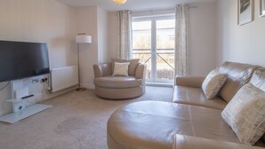 A modern living room with a large flat-screen TV, a round coffee table, a sofa, and a floor lamp. - Pass the Keys | Next to Braehead - Free Parking (Renfrew)