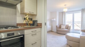 A modern kitchen with a gas stove, oven, and wooden cabinets. There is a dining area with a sofa and a lamp. - Pass the Keys | Next to Braehead - Free Parking (Renfrew)
