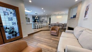 A modern living room with a sofa, a brown armchair, and a dining area in the background. - Resort-Style Home for Families: Pool, Theater, Arcade, Hot Tub, Central location (San Diego)