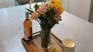 A kitchen with a marble countertop, a vase of flowers, a bottle, and a candle on a wooden tray. - Resort-Style Home for Families: Pool, Theater, Arcade, Hot Tub, Central location (San Diego)