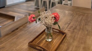 A modern kitchen with white cabinets, a wooden dining table with a vase of flowers, and pendant lights. - Resort-Style Home for Families: Pool, Theater, Arcade, Hot Tub, Central location (San Diego)