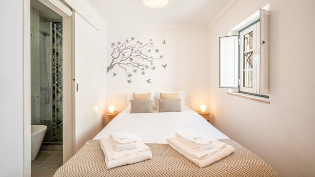 Habitación de hotel con cama, dos mesitas de noche con lámparas, ventana con vistas y un adhesivo de árbol en la pared.