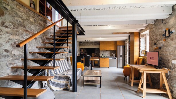 A modern interior with a staircase, a sofa, a dining table, and a kitchen area. - GuestReady – Rustic Charm in Peaceful Madeira (Porto da Cruz)