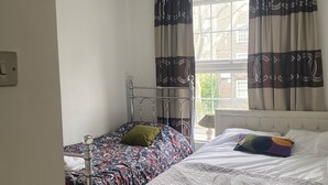 Un dormitorio con dos camas, una ventana con cortinas, una lámpara colgante y una mesita de noche con lámpara.