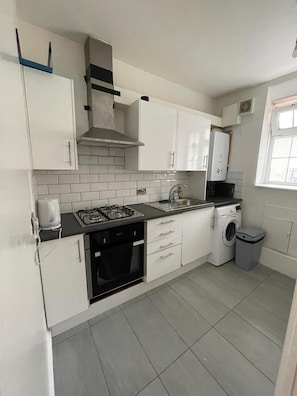 A compact kitchen with white cabinets, a gas stove, a microwave, and a washing machine.