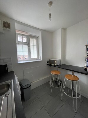 A kitchen with a window, two stools, a microwave, and a trash bin.