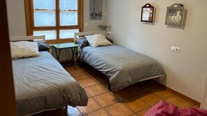 A small, clean room with two single beds, a small table, and a window with blinds. - APARTMENT IN MUROS DE NALÓN ASTURIAS (Muros de Nalón)