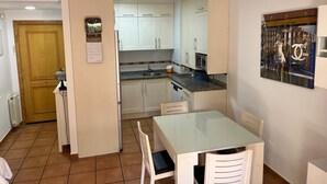 A compact kitchen with white cabinets, a small dining table with chairs, and a tiled floor. - APARTMENT IN MUROS DE NALÓN ASTURIAS (Muros de Nalón)