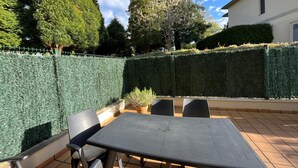 An outdoor patio with a table and chairs, surrounded by neatly trimmed hedges and trees. - APARTMENT IN MUROS DE NALÓN ASTURIAS (Muros de Nalón)
