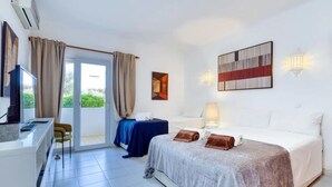 A hotel room with a bed, a desk, a chair, a TV, and a view of greenery outside. - Carvoeiro Pool House by Vacationy (Lagoa)
