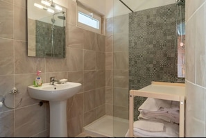 Un bagno con doccia, lavandino, specchio e porta asciugamani.