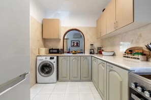 A compact kitchen with a washing machine, a microwave, and a sink. There is a wooden cabinet above the sink and a spice rack on the countertop. - Carvoeiro Pool House by Vacationy (Lagoa)