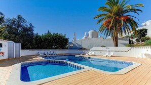 A pool area with a wooden deck, lounge chairs, and a palm tree. - Carvoeiro Pool House by Vacationy (Lagoa)