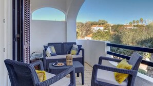 A balcony with wicker furniture, a table with a plate of food, and a view of houses and trees. - Carvoeiro Pool House by Vacationy (Lagoa)