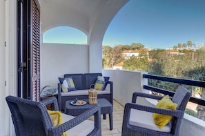 Un balcon agrémenté de meubles en osier, une table avec une assiette de nourriture et une vue sur des maisons et des arbres.