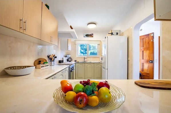Una cucina moderna con mobili chiari in legno, un piano di lavoro bianco e una ciotola di frutta.