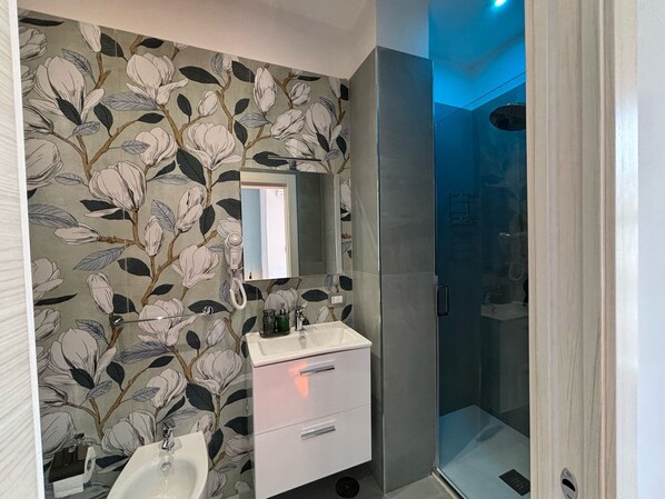 Une salle de bain avec un papier peint à motifs floraux, un miroir, un lavabo et un espace douche.