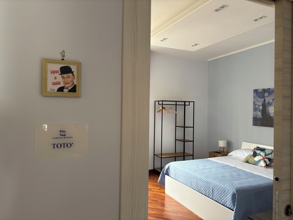 A hotel room with a bed, a wardrobe, a framed picture, and a painting on the wall. - Caridei Rooms (Naples)