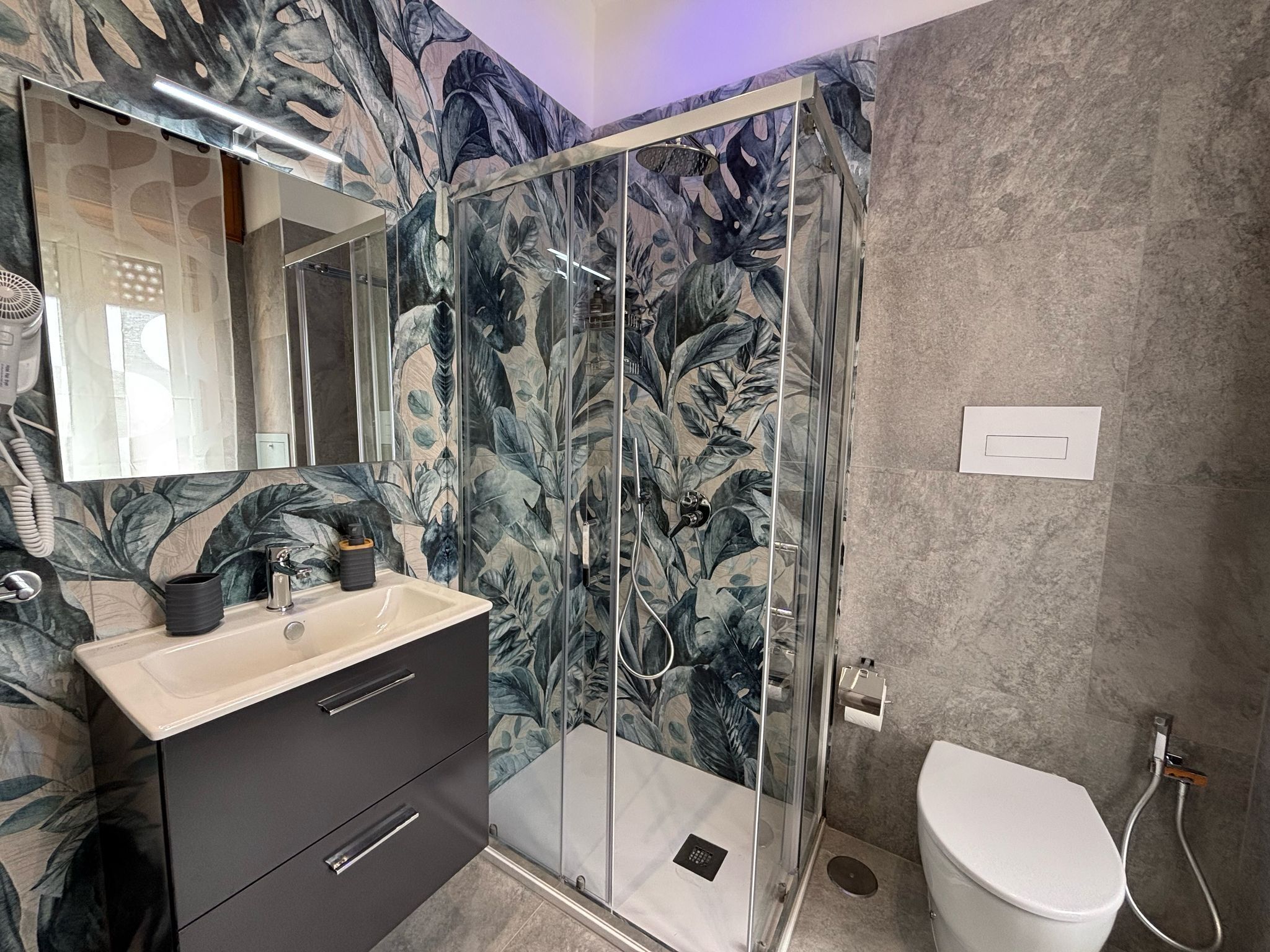 Une salle de bain moderne avec une douche à parois de verre, un lavabo avec un miroir au-dessus et des toilettes.