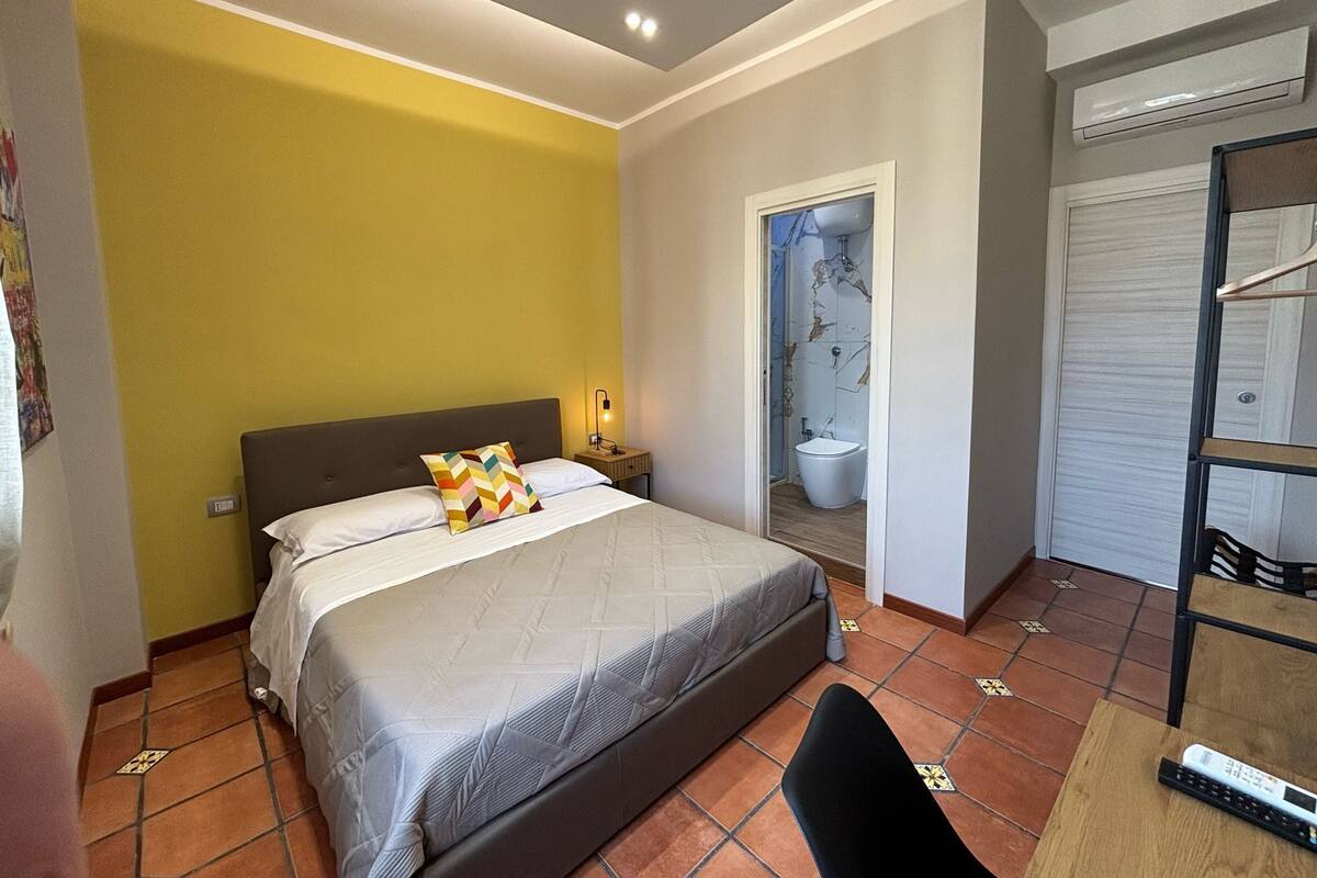 A hotel room with a bed, a nightstand, a bathroom with a toilet and sink, and a wardrobe.