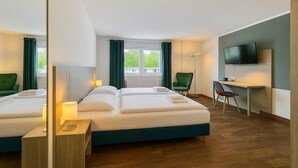 Quarto de hotel com duas camas, uma escrivaninha, uma cadeira, televisão e vista para o verde lá fora.