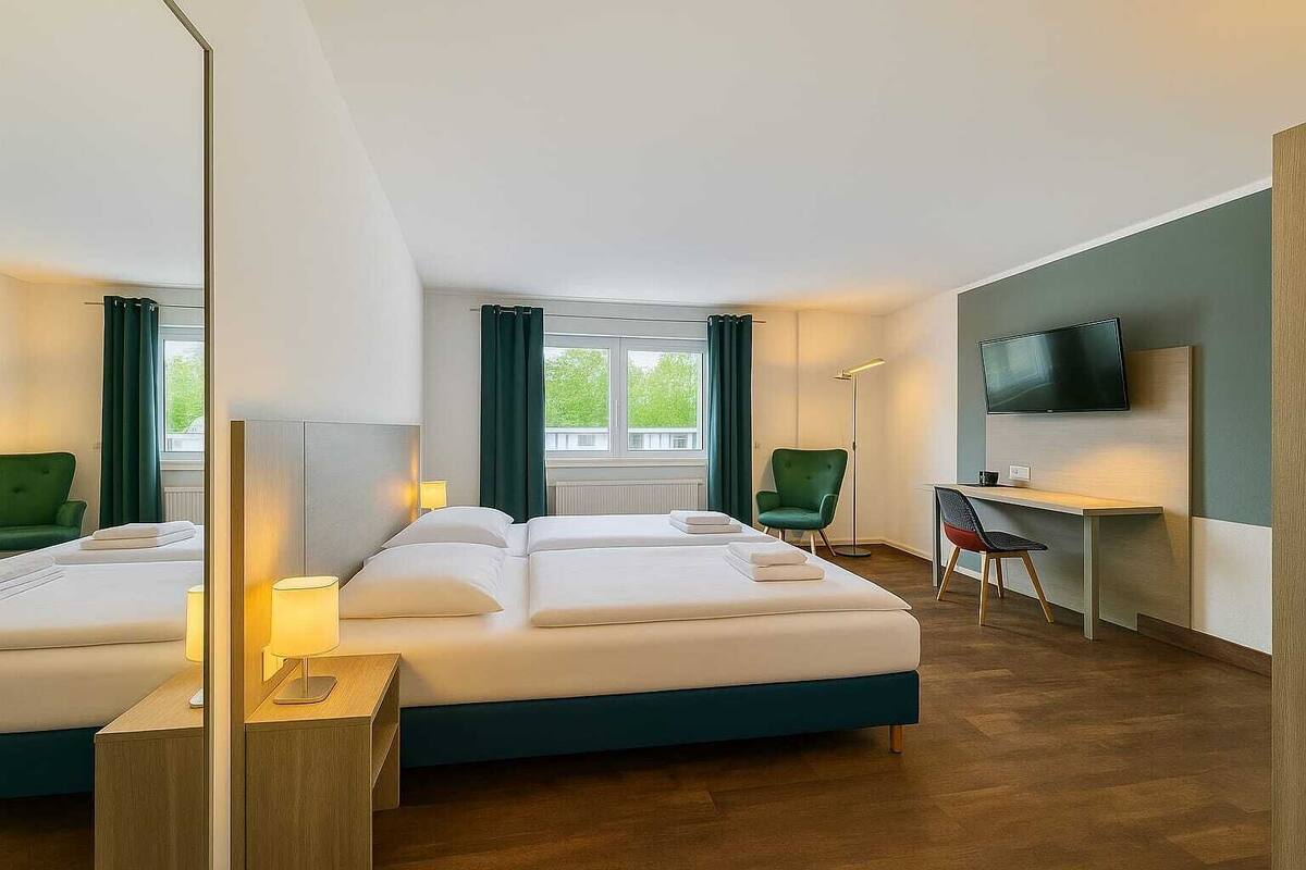 Une chambre d’hôtel avec deux lits, un bureau, une chaise, une télévision et une vue sur la verdure.