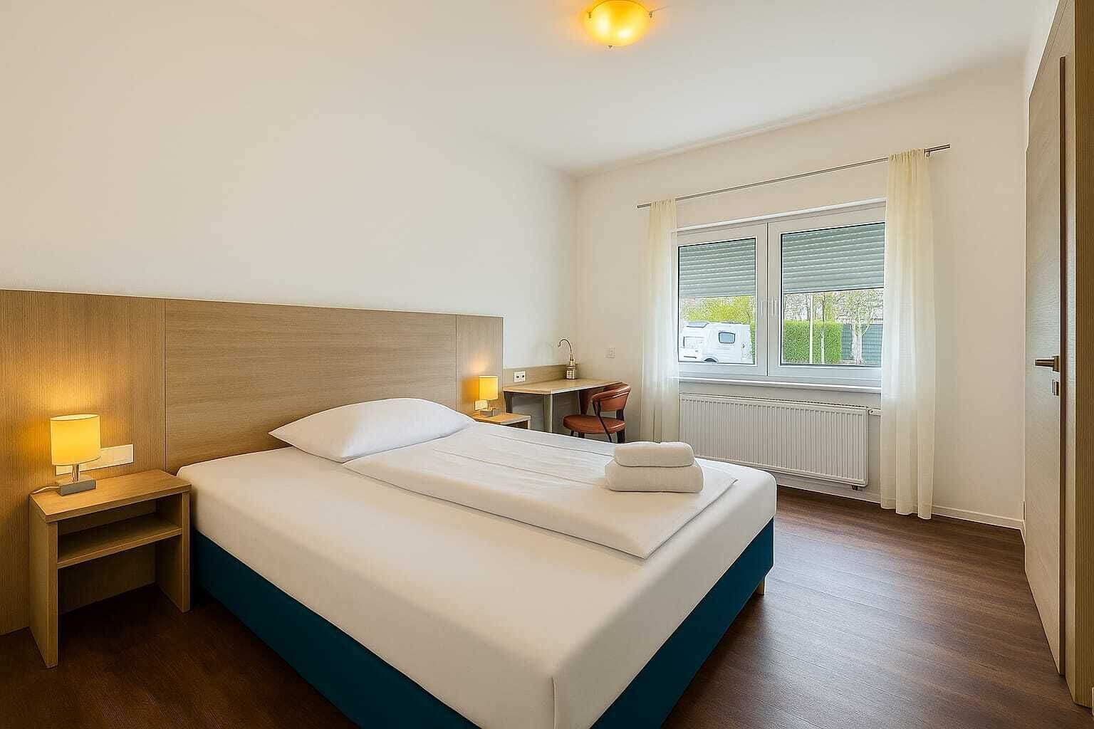 Ein Hotelzimmer mit Bett, Nachttischen, einem Fenster mit Vorhängen und einem Heizkörper.