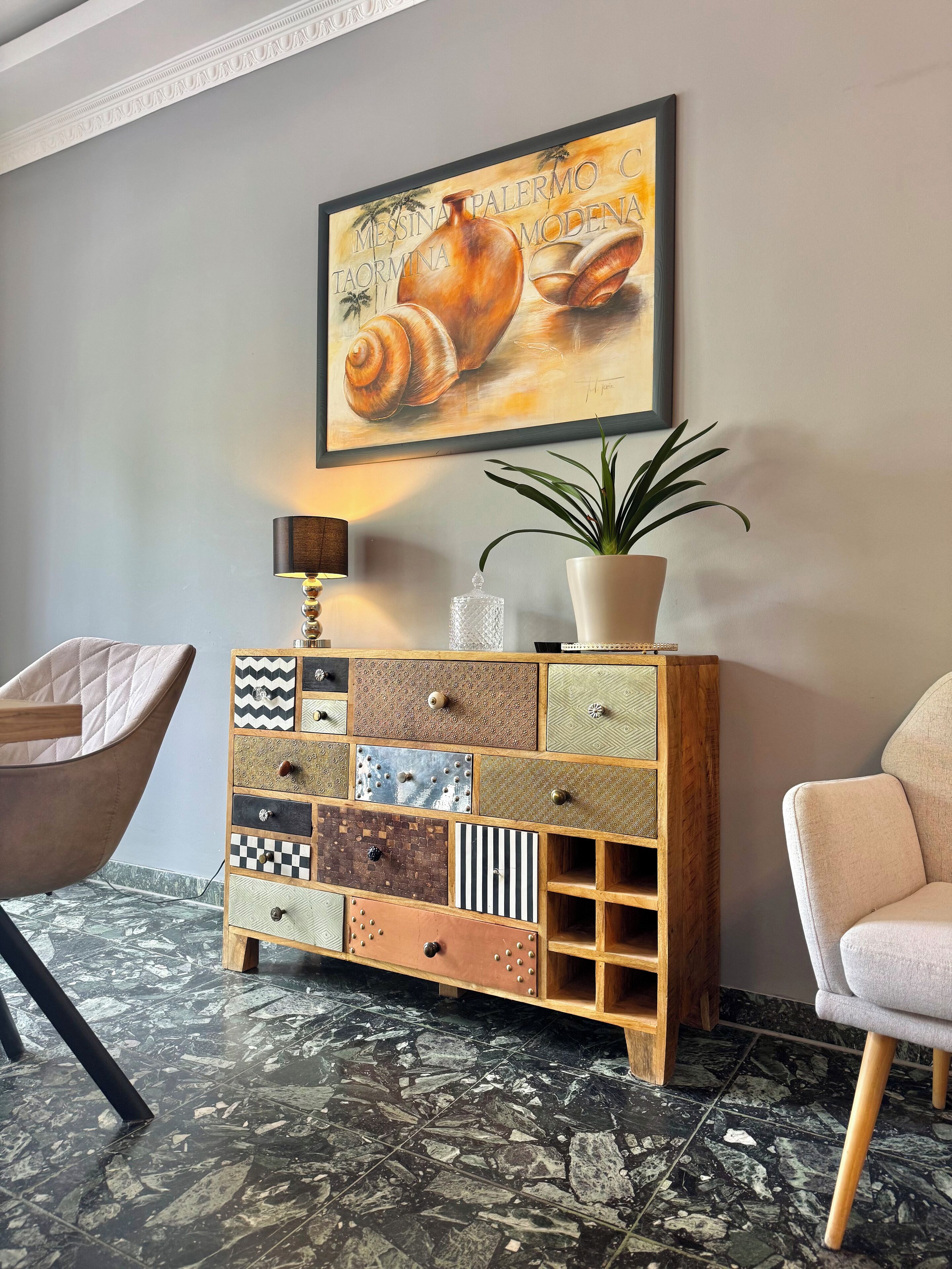 A room with a marble floor, a wooden cabinet with various patterns, a framed artwork above it, and a potted plant.