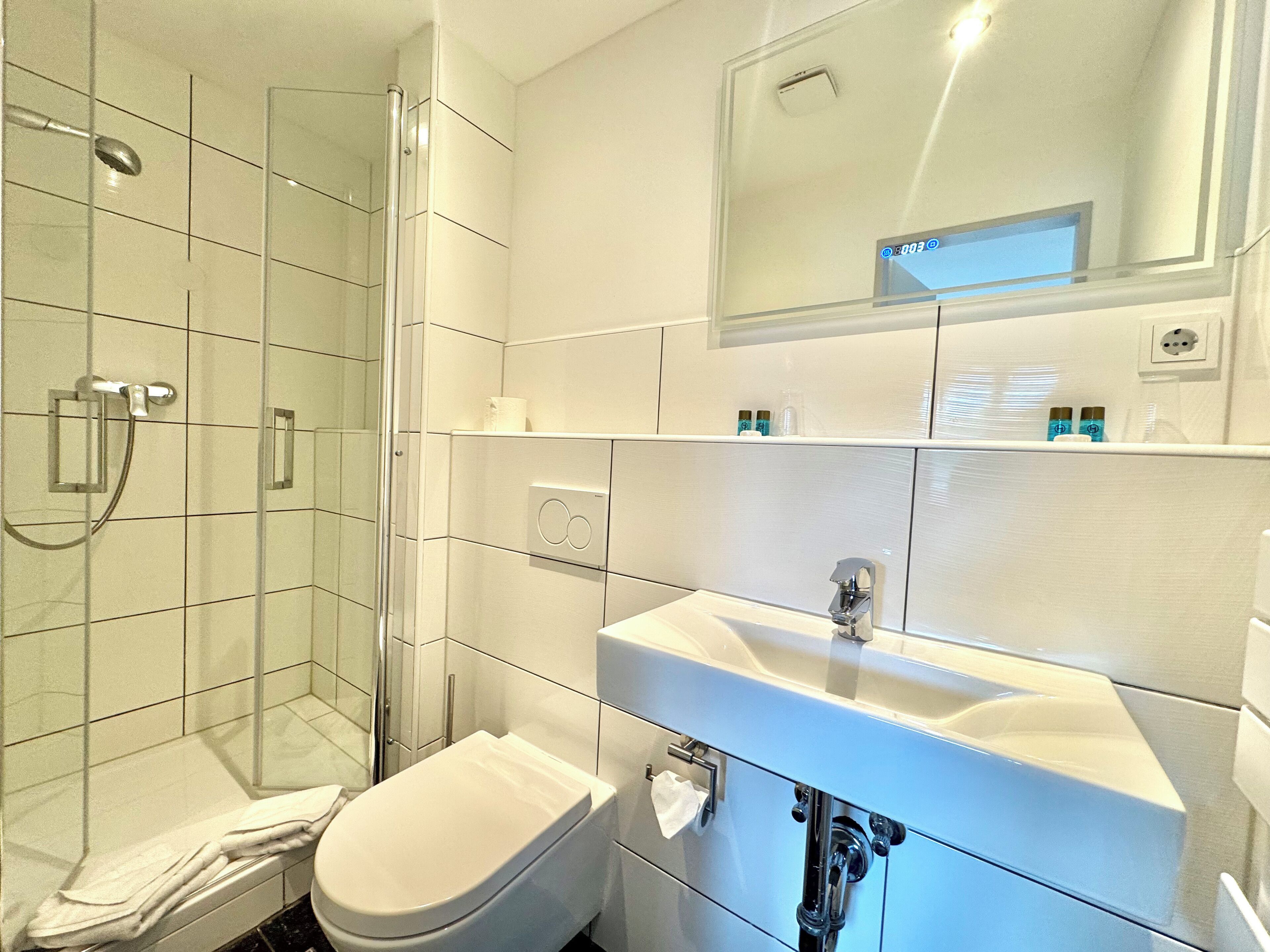 Un baño moderno con ducha de vidrio, lavamanos blanco y retrete.